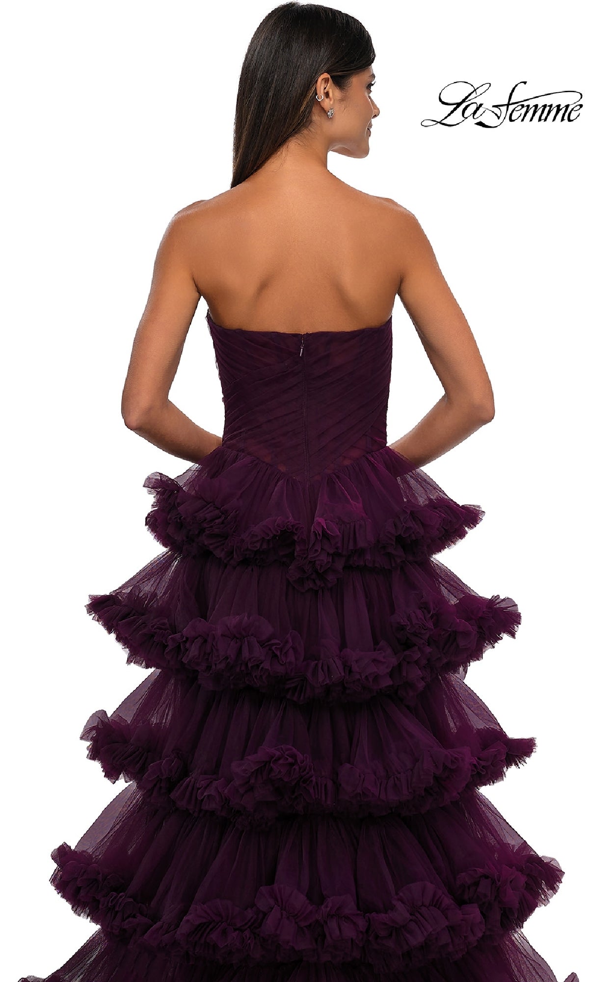 A woman with long dark hair models the La Femme 32721 Strapless Ruffled Prom Ball Gown, a purple tiered dress with elegant ruffled layers, shown from the back against a white background.